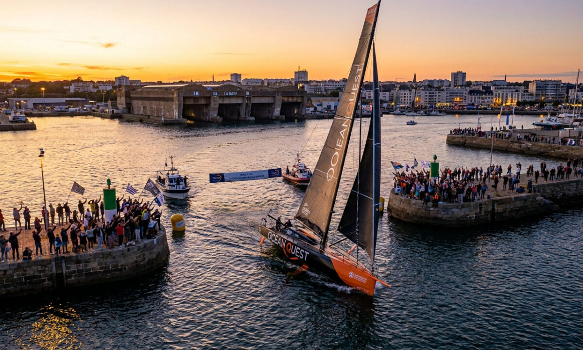 Un voilier de course Ocean Quest franchit l'entrée du port de Lorient sous les acclamations d'une foule au coucher du soleil.